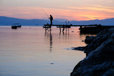 Silhouette man fishing in sea against sky during sunset