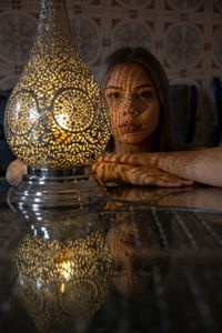 Portrait of young woman sitting against illuminated lamp at home