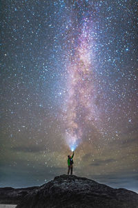 Full length of man with flashlight standing on rock against sky at night