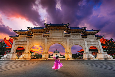 Rear view of woman standing by building against cloudy sky