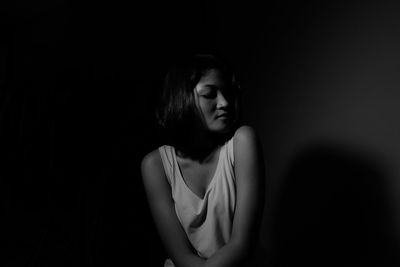 Young woman sitting against black background