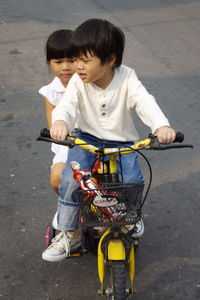 Cute boy riding tricycle with sister on road