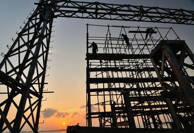 Low angle view of workers on silhouette scaffolding against sky during sunset