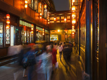 People walking on illuminated street amidst buildings at night
