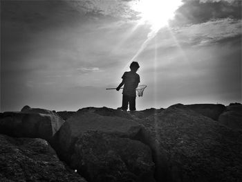 Boy standing on rock against sky