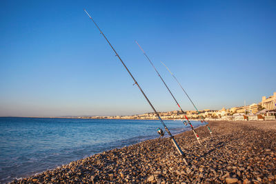 Fishing rods on a pebble beach on promenade des anglais at dawn, nice, france