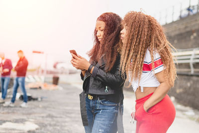 Mother looking at daughter using mobile phone on street