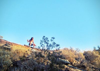 Low angle view of man crouching on hill against clear sky