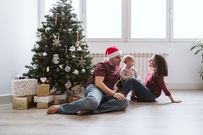 Mother breastfeeding her baby girl at home by the christmas tree. family time