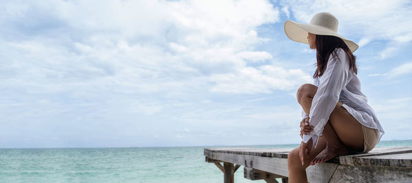 Full length of woman sitting by sea against sky