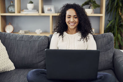 Young woman using phone while sitting on sofa at home