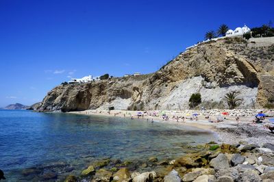 People on cliff by sea against clear blue sky