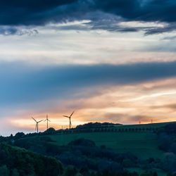 Windmill on landscape against sky at sunset