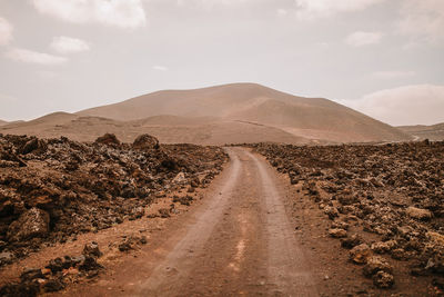 Dirt road amidst land against sky