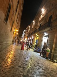 People walking on illuminated street amidst buildings at night