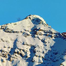 Low angle view of snow covered mountain against blue sky