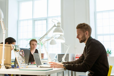 Confident young businessman using laptop while sitting at desk in creative office