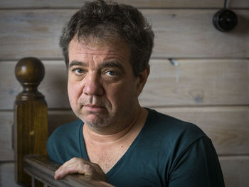Portrait of mature man sitting by wooden railing at home