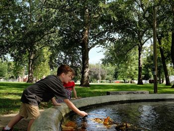 Cute brother and sister playing near pond in park against trees