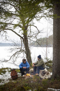 Male friends talking with each other while sitting by bonfire during winter