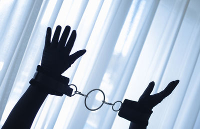 Cropped hands of silhouette person with handcuffs against window