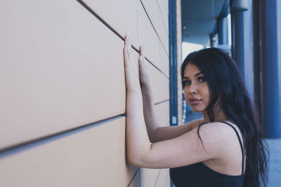 Side view portrait of young woman standing by wall