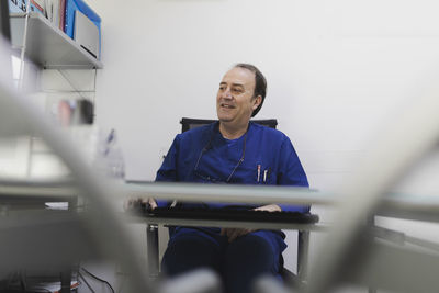 Adult cheerful male doctor in uniform working at computer in veterinary clinic