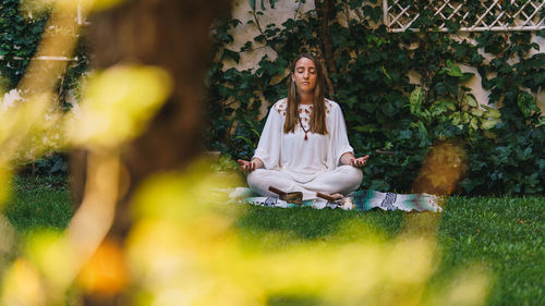 Young woman sitting on plants against trees