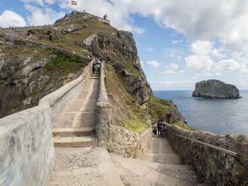 People on mountain by sea against sky in the spanish island of gaztelugatxe