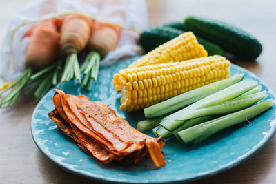 Fresh cooked carrot bacon lies on a turquoise plate with corn and cucumber.  meat replacement, snack