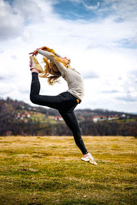 Full length of young woman jumping on field against sky