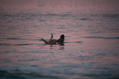 Silhouette person swimming in sea against sky during sunset