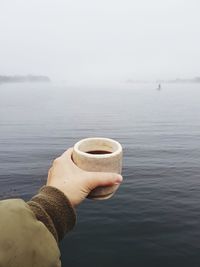 Cropped image of person holding coffee cup sea