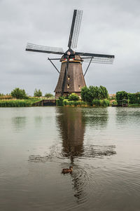 Traditional windmill by lake against sky