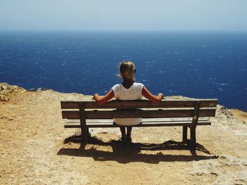 Rear view of woman sitting on bench looking at sea