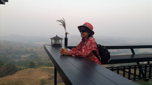 Woman sitting on railing against mountain