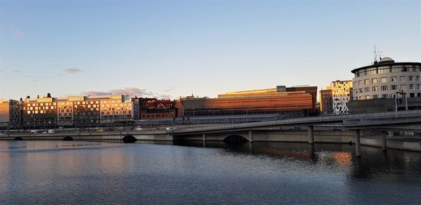 Bridge over river against buildings in city at sunset
