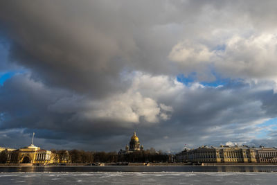 Buildings at waterfront against cloudy sky