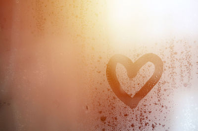 Close-up of heart shape on condensed glass during sunset