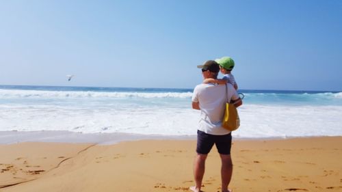 Rear view of man standing on beach against clear sky