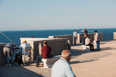 Rear view of people at beach against clear sky