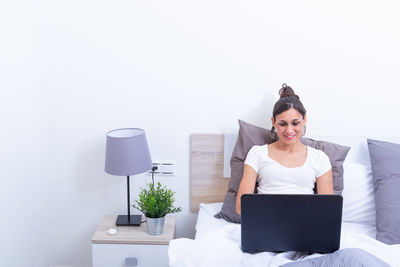 Young woman using laptop while sitting against white background