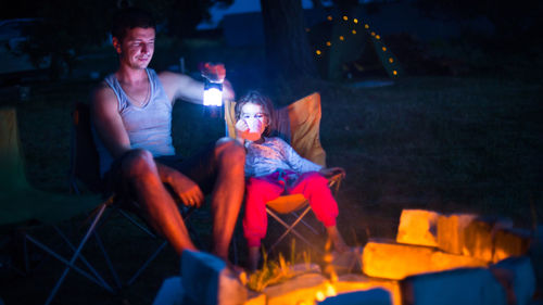 Midsection of woman sitting on illuminated fire at night