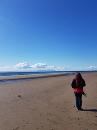 Rear view of woman standing on beach against blue sky