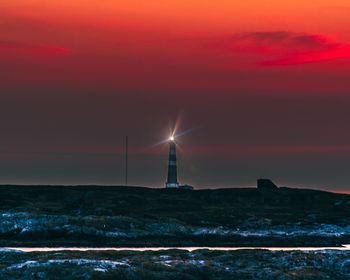 Lighthouse by sea against sky during sunset