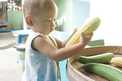 Side view of cute baby boy holding corn at home