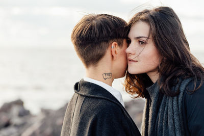 Lesbian women embracing while standing against sea