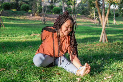Beautiful young woman with long african braids is doing yoga outside in a park. 