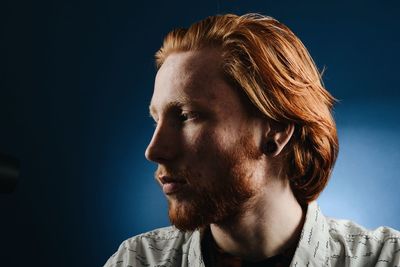 Close-up of man looking away while sitting against blue background