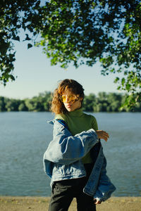 Side view of young woman standing against lake